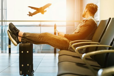 キャリーケースに足を置いて飛行機を眺める男性
